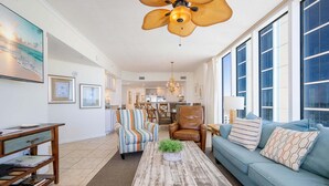 Ein geräumiges Wohnzimmer mit großem Fenster, Deckenventilator und Couchtisch mit Pflanze.