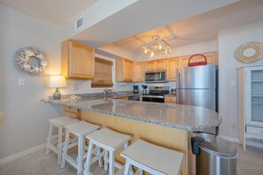 Una cocina con encimeras de granito, armarios de madera, refrigerador de acero inoxidable y microondas integrado.
