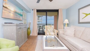 Un salon doté d’un ventilateur de plafond, d’un canapé, d’une table basse sur laquelle se trouve une statuette de tortue, d’un fauteuil, d’une armoire, d’un tableau et d’une vue sur le balcon.