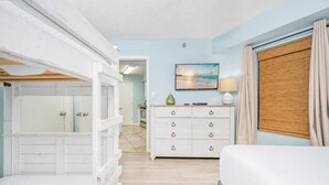 Une chambre à coucher avec un lit, une commode, un tableau et une fenêtre avec des rideaux.