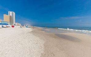 A beach with a sandy shore, a few umbrellas, and a building in the background. - Gulf Side Townhomes 20 2 Bedroom Condo (Gulf Shores)