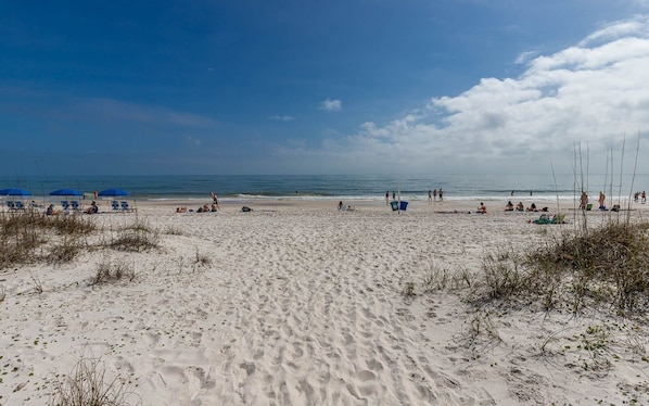 A sandy beach with people sunbathing and swimming.