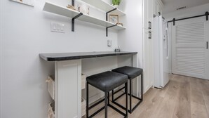 A modern kitchen with white cabinetry, black bar stools, and open shelving with decorative items. - Gulf Side Townhomes 20 2 Bedroom Condo (Gulf Shores)