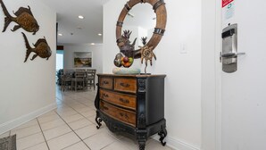 A hallway with a wooden cabinet, a decorative mirror, and wall art. - Lighthouse 215 3 Bedroom Condo (Gulf Shores)
