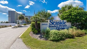 A sign for Seaside Beach & Club with a number 24522, surrounded by greenery and palm trees. - Seaside Beach & Racquet 5916 2 Bedroom Condo (Orange Beach)
