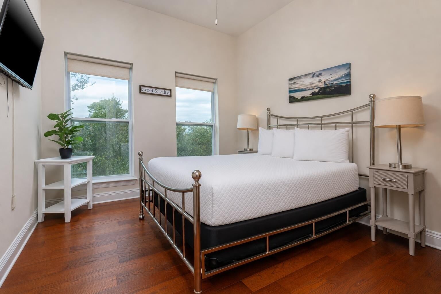 Una camera da letto con un letto, comodini, una TV, una finestra e un quadro.