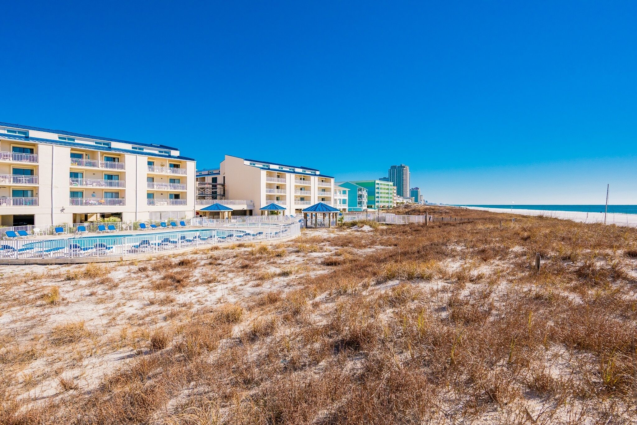 Un hotel frente a la playa con varios balcones, zona de piscina y servicios en la costa.