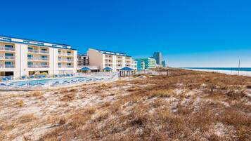 Un hotel frente a la playa con varios balcones, zona de piscina y servicios en la costa.