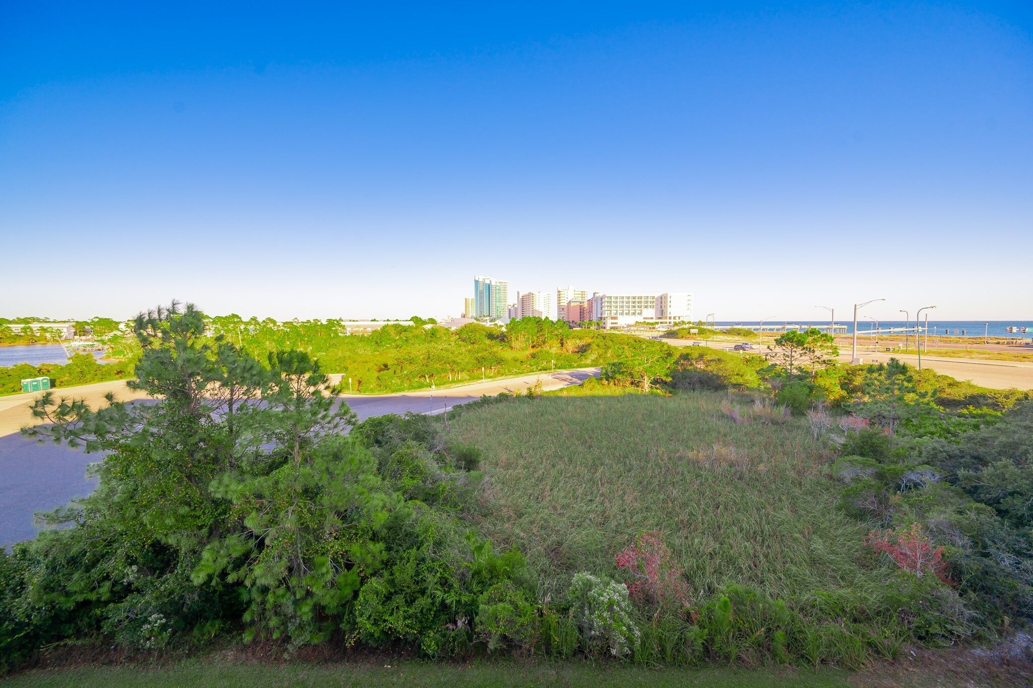 A coastal cityscape with modern high-rise buildings, a clear sky, and a lush green area in the foreground.