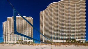 Dos hoteles de gran altura con fachada curva, ubicados en una playa de arena con cielo azul despejado.