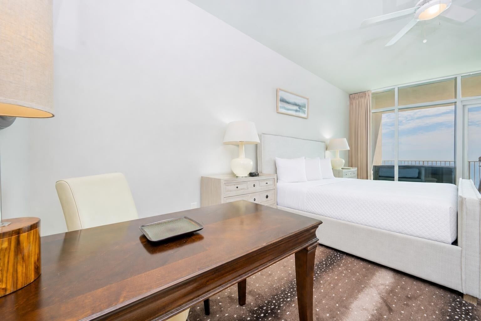 A hotel room with a bed, a desk, a chair, a nightstand, and a window with a view.