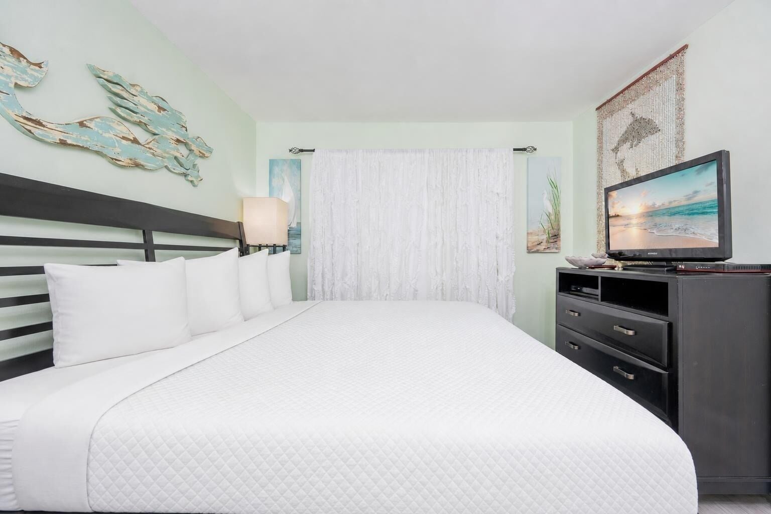 A neatly made bed with white bedding, a headboard, and a wall-mounted TV.