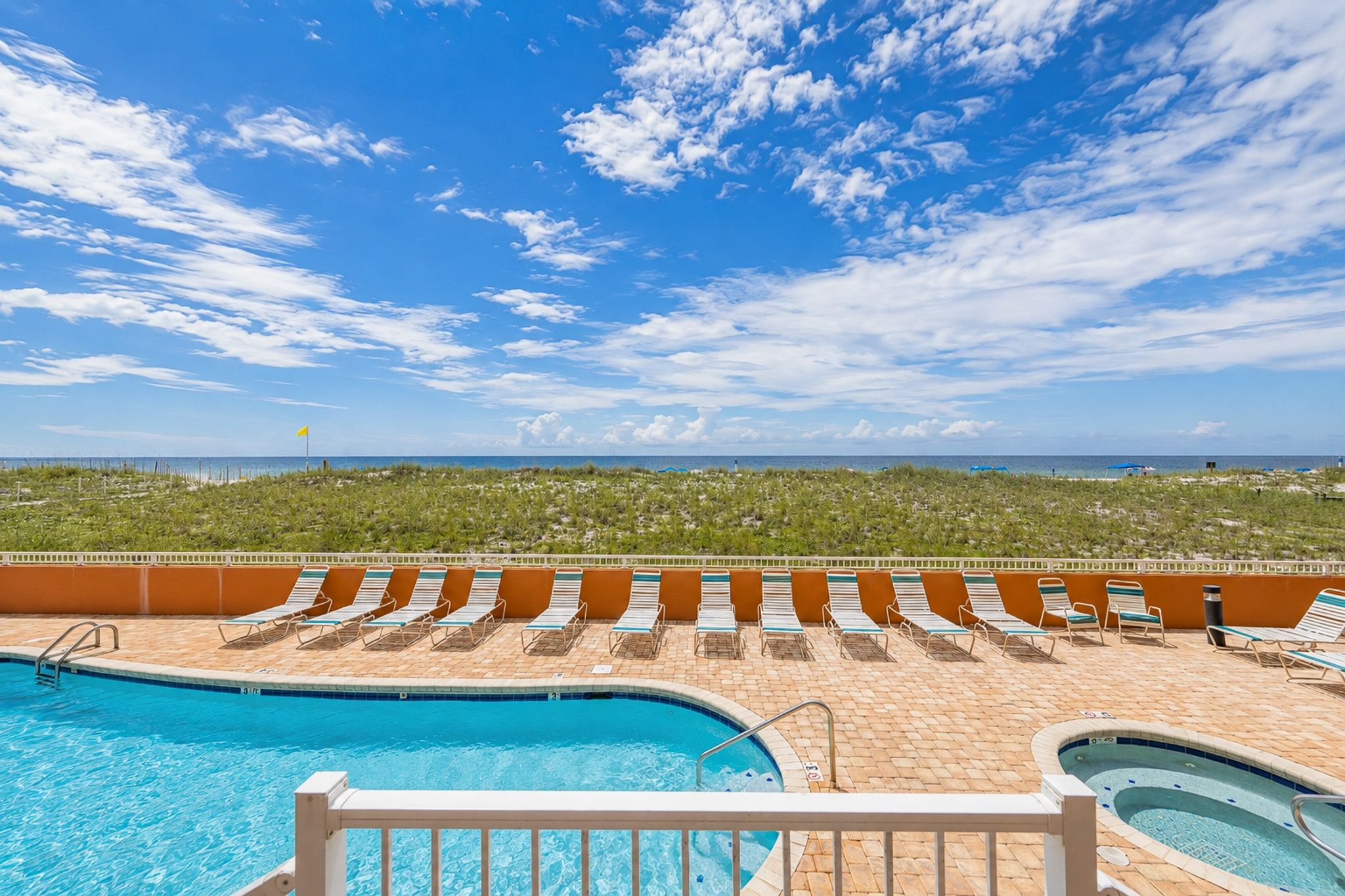 A pool area with multiple lounge chairs and a view of the ocean.