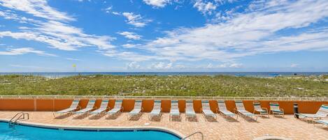 A pool area with multiple lounge chairs and a view of the ocean.