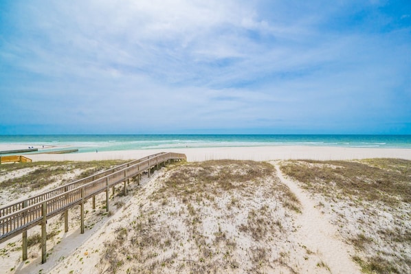 Une plage avec une promenade en bois qui mène à l’eau, des dunes de sable et un ciel dégagé.