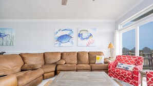 A living room with a brown leather sectional sofa, a wooden coffee table, and a red patterned armchair. There are three wall-mounted artworks depicting fish. - Funspot 1713 5 Bedroom Home (Gulf Shores)
