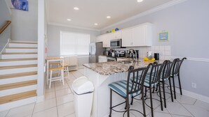 A kitchen with white cabinets, a granite countertop, and a dining area with striped chairs.