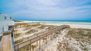 A beach view with a wooden boardwalk, sandy dunes, and a building with a balcony. - Funspot 1713 5 Bedroom Home (Gulf Shores)