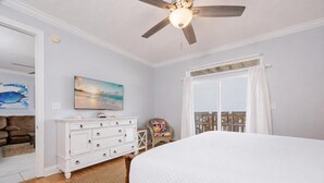 A bedroom with a bed, a dresser, a chair, a ceiling fan, and a painting on the wall. - Funspot 1713 5 Bedroom Home (Gulf Shores)