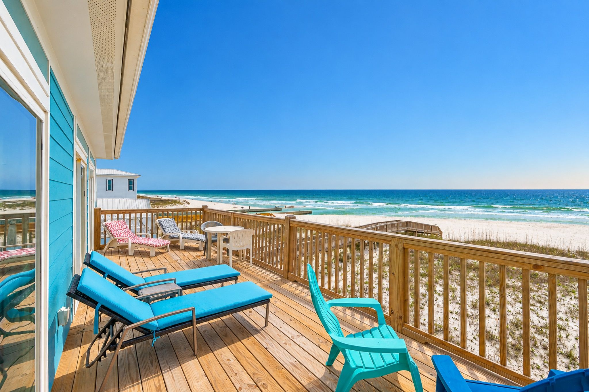 A wooden deck with blue lounge chairs and a wooden railing overlooking a beach.