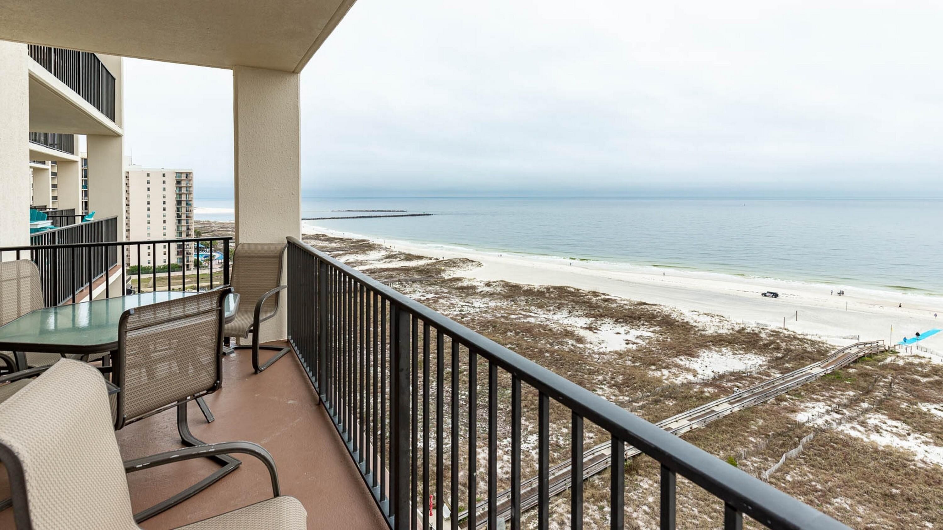 A balcony with a table and chairs overlooking a beach and ocean.