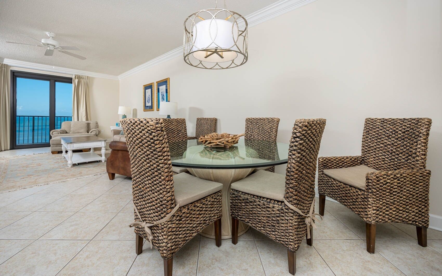 A dining area with wicker chairs, a glass table, and a ceiling fan.