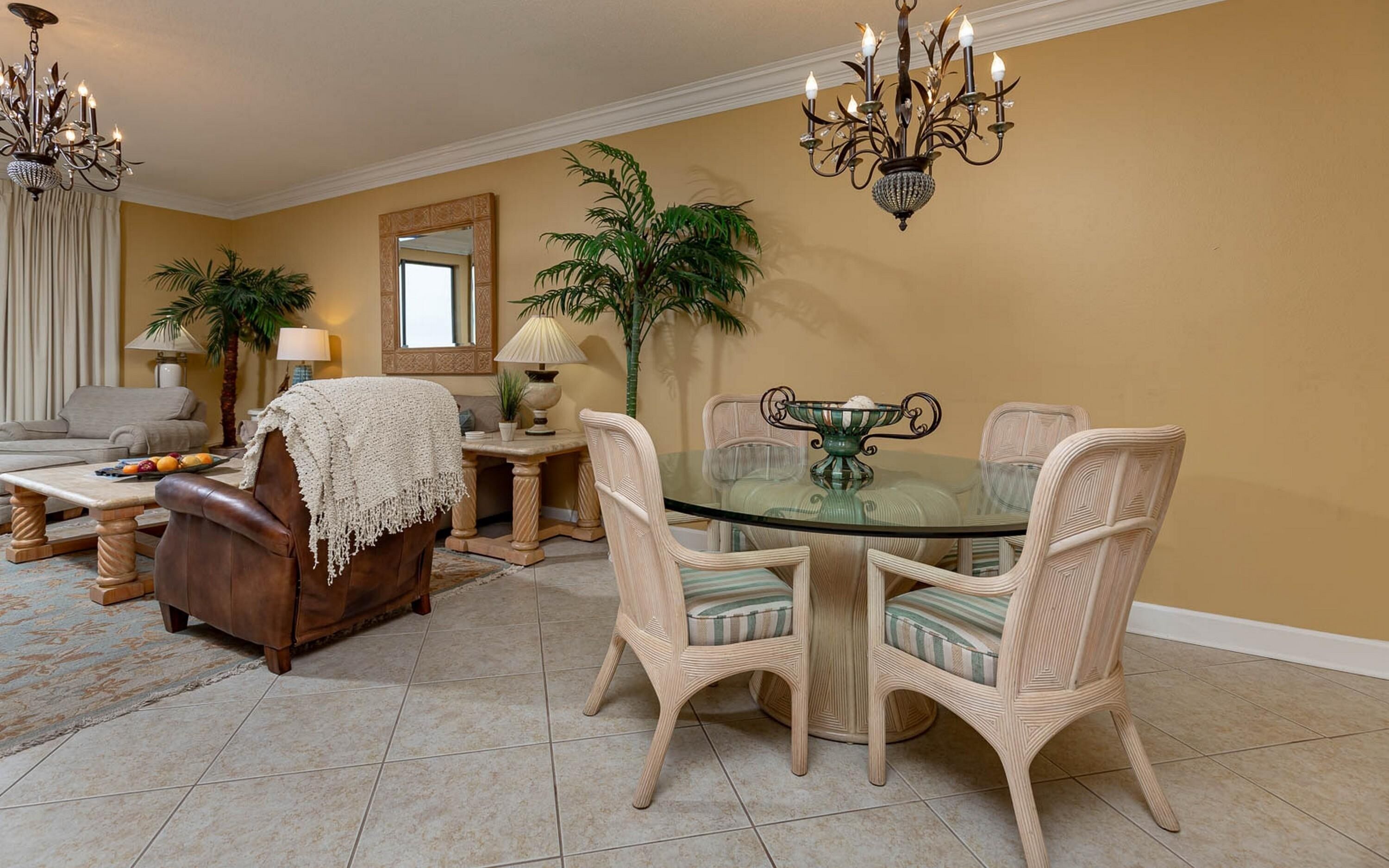 A dining area with a glass table surrounded by wicker chairs, a brown sofa, and a coffee table with fruits.