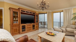 A spacious living room with a large flat-screen TV, wooden entertainment unit, leather sofa, and a dining table with fruit. - Phoenix VII by Brett/Robinson Vacations (Orange Beach)