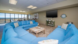 A spacious living area with a large blue sectional sofa, a wooden coffee table, and a flat-screen TV mounted on the wall. - Phoenix VII by Brett/Robinson Vacations (Orange Beach)