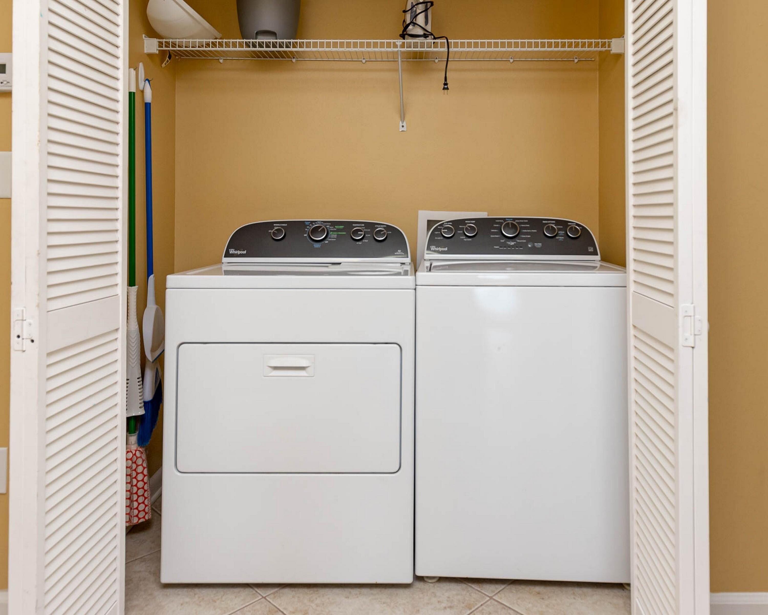 A laundry room with two stacked Whirlpool dryers, a white shelf above, and a white door with louvered panels.