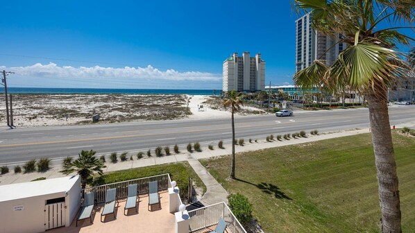Un hôtel situé en bord de mer, avec une route au premier plan, un palmier et une vue dégagée sur l’océan.