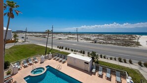 A pool area with lounge chairs, a small pool, and a view of the beach and ocean.