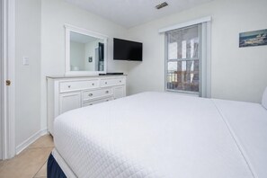 A bedroom with a bed, a dresser, a television, and a window with blinds. - Grand Beach Resort 308 1 Bedroom Condo (Gulf Shores)