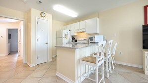 A kitchen with white cabinets, a built-in island with bar stools, a microwave, and a refrigerator.