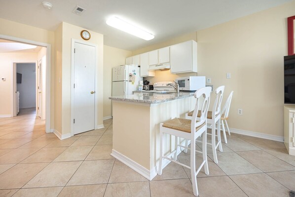 A kitchen with white cabinets, a built-in island with bar stools, a microwave, and a refrigerator. - Grand Beach Resort 308 1 Bedroom Condo (Gulf Shores)