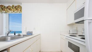 A compact kitchen with a window, a microwave, a stove, and a sink. - Royal Palms 708 2 Bedroom Condo (Gulf Shores)