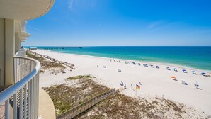 A beach view from a balcony with a wooden deck, a pier in the distance, and beach umbrellas.