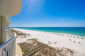 A beach view from a balcony with a wooden deck, a pier in the distance, and beach umbrellas.