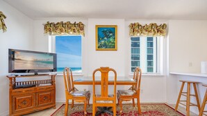 A dining area with a TV, wooden dining table, chairs, and a red patterned rug.