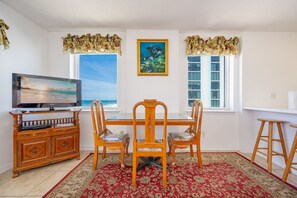 A dining area with a TV, wooden dining table, chairs, and a red patterned rug.