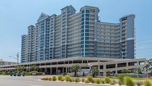 A multi-story hotel with a modern design, featuring a covered parking area and a landscaped entrance. - Lighthouse 814 2 Bedroom Condo (Gulf Shores)