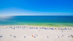 A beach with clear blue water, sandy shore, and beach umbrellas.