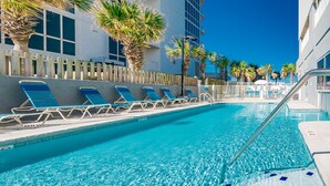 A swimming pool with lounge chairs, palm trees, and a building in the background.