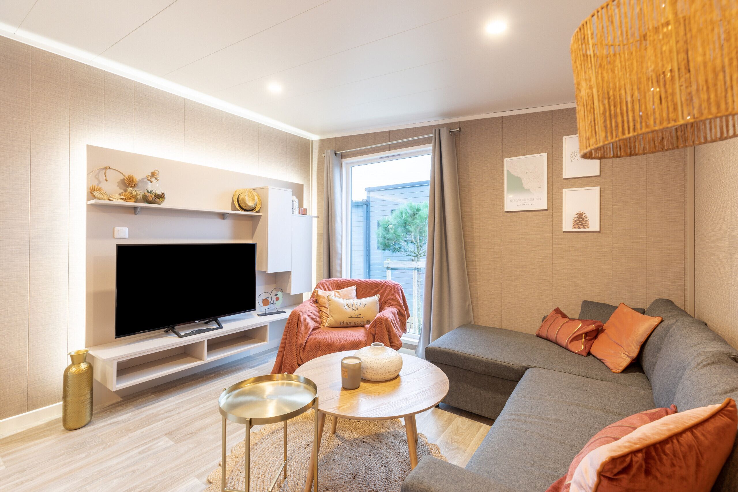 Un salon moderne avec un téléviseur à écran plat, un canapé gris, un fauteuil rouge et une petite table basse ronde.