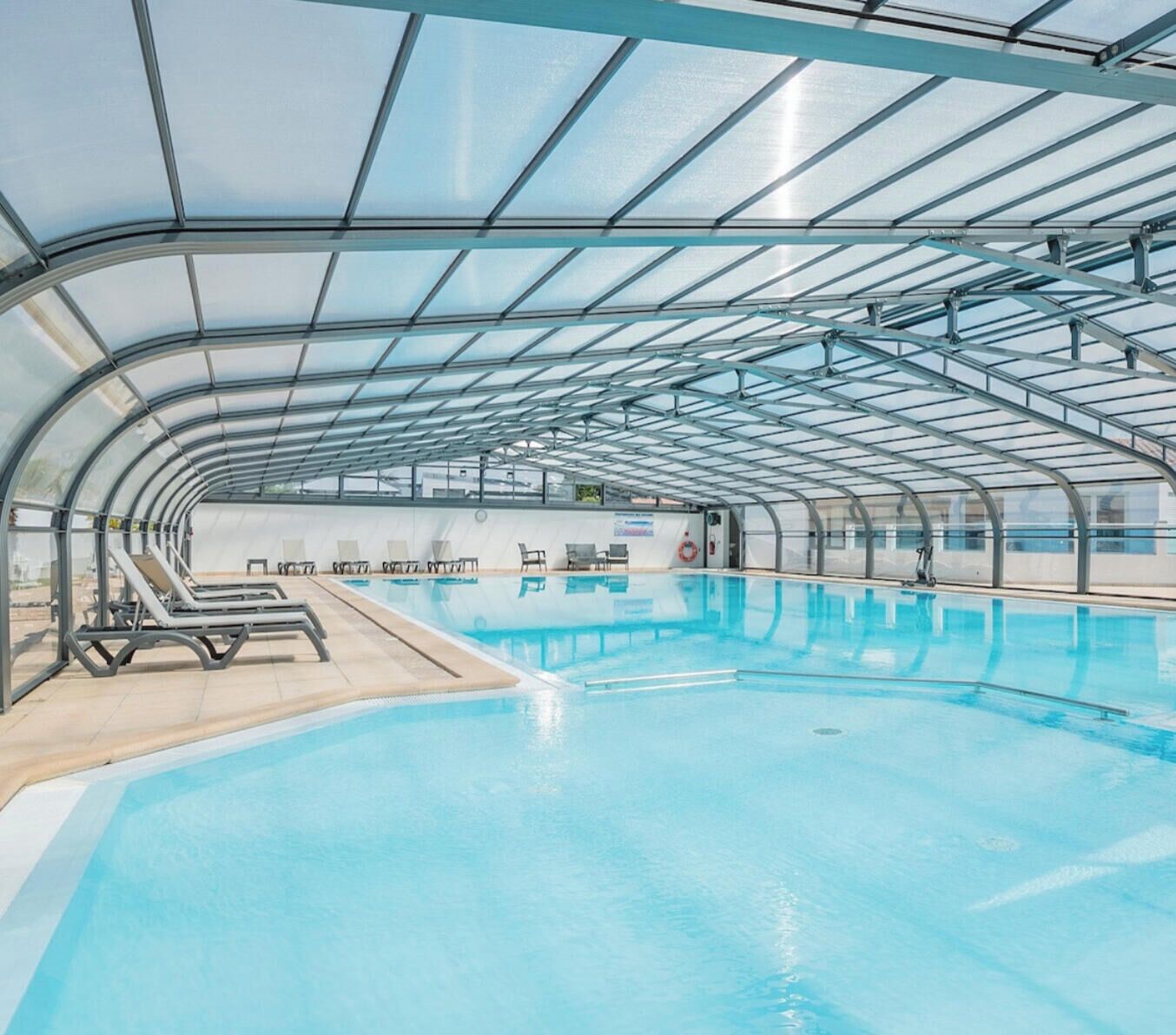 Une piscine intérieure dotée d’un toit en verre, de chaises longues et d’une bouée de sauvetage.