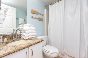 Een badkamer met een wastafel op een granieten blad, een wit toilet en een douchegordijn.