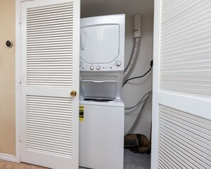 Een kleine wasruimte met een voorlader wasmachine en droger, een deur met hendel en een zichtbare slang.