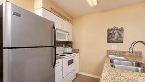 A compact kitchen with a stainless steel refrigerator, a microwave, a stove, and a sink. - Royal Palms 1207 1 Bedroom Condo (Gulf Shores)