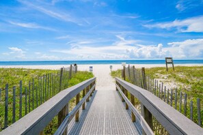 Une promenade en bois qui mène à une plage, avec un ciel dégagé.