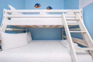 Un lit superposé avec une échelle, du linge de lit blanc et deux éléments de décoration murale.